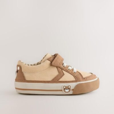 These adorable low-top trainers blend soft textures and neutral tones, featuring a large star graphic and multiple charming bear motifs for a fun, stylish look, secured by a single hook-and-loop strap. Brand: Next UK Mixed Media Upper: The low-cut body combines smooth light beige/cream synthetic material on the side and vamp, with tan/brown faux suede/nubuck overlays on the toe cap, eyelet area, and strap. Star Graphic Detail: The side panel features a large star-shaped graphic in the smooth light beige material, sharply defined by the darker tan stitching and overlay edges. Hybrid Closure: The shoe includes fixed, wide cream/white laces for a traditional look, secured by a single, adjustable hook-and-loop (Velcro) strap made of the tan faux suede. Multiple Bear Motifs: The heel patch features a sweet embroidered bear face. A second, small embossed bear face graphic is visible on the outer sidewall of the gum rubber sole, adding character. Gum Rubber Sole: The trainers are set on a flat, thick gum/natural colored rubber sole with a classic chevron/zig-zag tread pattern. The sidewall features a subtle contrast stripe. Color: Upper is predominantly Light Beige / Cream with Tan / Brown overlays. Sole is Gum / Natural Brown. Lining is Beige and White Striped. A comfortable and charming low-top trainer featuring a multi-tonal neutral upper, a star graphic, and playful bear character accents.
