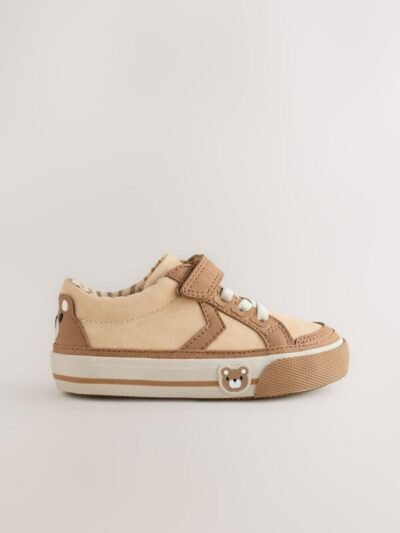 These adorable low-top trainers blend soft textures and neutral tones, featuring a large star graphic and multiple charming bear motifs for a fun, stylish look, secured by a single hook-and-loop strap. Brand: Next UK Mixed Media Upper: The low-cut body combines smooth light beige/cream synthetic material on the side and vamp, with tan/brown faux suede/nubuck overlays on the toe cap, eyelet area, and strap. Star Graphic Detail: The side panel features a large star-shaped graphic in the smooth light beige material, sharply defined by the darker tan stitching and overlay edges. Hybrid Closure: The shoe includes fixed, wide cream/white laces for a traditional look, secured by a single, adjustable hook-and-loop (Velcro) strap made of the tan faux suede. Multiple Bear Motifs: The heel patch features a sweet embroidered bear face. A second, small embossed bear face graphic is visible on the outer sidewall of the gum rubber sole, adding character. Gum Rubber Sole: The trainers are set on a flat, thick gum/natural colored rubber sole with a classic chevron/zig-zag tread pattern. The sidewall features a subtle contrast stripe. Color: Upper is predominantly Light Beige / Cream with Tan / Brown overlays. Sole is Gum / Natural Brown. Lining is Beige and White Striped. A comfortable and charming low-top trainer featuring a multi-tonal neutral upper, a star graphic, and playful bear character accents.