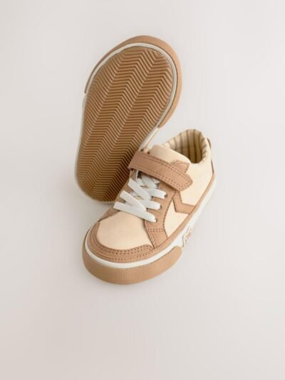 These adorable low-top trainers blend soft textures and neutral tones, featuring a large star graphic and multiple charming bear motifs for a fun, stylish look, secured by a single hook-and-loop strap. Brand: Next UK Mixed Media Upper: The low-cut body combines smooth light beige/cream synthetic material on the side and vamp, with tan/brown faux suede/nubuck overlays on the toe cap, eyelet area, and strap. Star Graphic Detail: The side panel features a large star-shaped graphic in the smooth light beige material, sharply defined by the darker tan stitching and overlay edges. Hybrid Closure: The shoe includes fixed, wide cream/white laces for a traditional look, secured by a single, adjustable hook-and-loop (Velcro) strap made of the tan faux suede. Multiple Bear Motifs: The heel patch features a sweet embroidered bear face. A second, small embossed bear face graphic is visible on the outer sidewall of the gum rubber sole, adding character. Gum Rubber Sole: The trainers are set on a flat, thick gum/natural colored rubber sole with a classic chevron/zig-zag tread pattern. The sidewall features a subtle contrast stripe. Color: Upper is predominantly Light Beige / Cream with Tan / Brown overlays. Sole is Gum / Natural Brown. Lining is Beige and White Striped. A comfortable and charming low-top trainer featuring a multi-tonal neutral upper, a star graphic, and playful bear character accents.