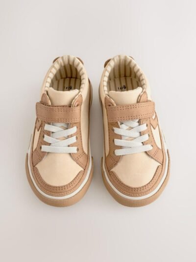 These adorable low-top trainers blend soft textures and neutral tones, featuring a large star graphic and multiple charming bear motifs for a fun, stylish look, secured by a single hook-and-loop strap. Brand: Next UK Mixed Media Upper: The low-cut body combines smooth light beige/cream synthetic material on the side and vamp, with tan/brown faux suede/nubuck overlays on the toe cap, eyelet area, and strap. Star Graphic Detail: The side panel features a large star-shaped graphic in the smooth light beige material, sharply defined by the darker tan stitching and overlay edges. Hybrid Closure: The shoe includes fixed, wide cream/white laces for a traditional look, secured by a single, adjustable hook-and-loop (Velcro) strap made of the tan faux suede. Multiple Bear Motifs: The heel patch features a sweet embroidered bear face. A second, small embossed bear face graphic is visible on the outer sidewall of the gum rubber sole, adding character. Gum Rubber Sole: The trainers are set on a flat, thick gum/natural colored rubber sole with a classic chevron/zig-zag tread pattern. The sidewall features a subtle contrast stripe. Color: Upper is predominantly Light Beige / Cream with Tan / Brown overlays. Sole is Gum / Natural Brown. Lining is Beige and White Striped. A comfortable and charming low-top trainer featuring a multi-tonal neutral upper, a star graphic, and playful bear character accents.